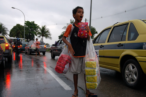 Criança vendendo pipoca no trânsito em um dia chuvoso