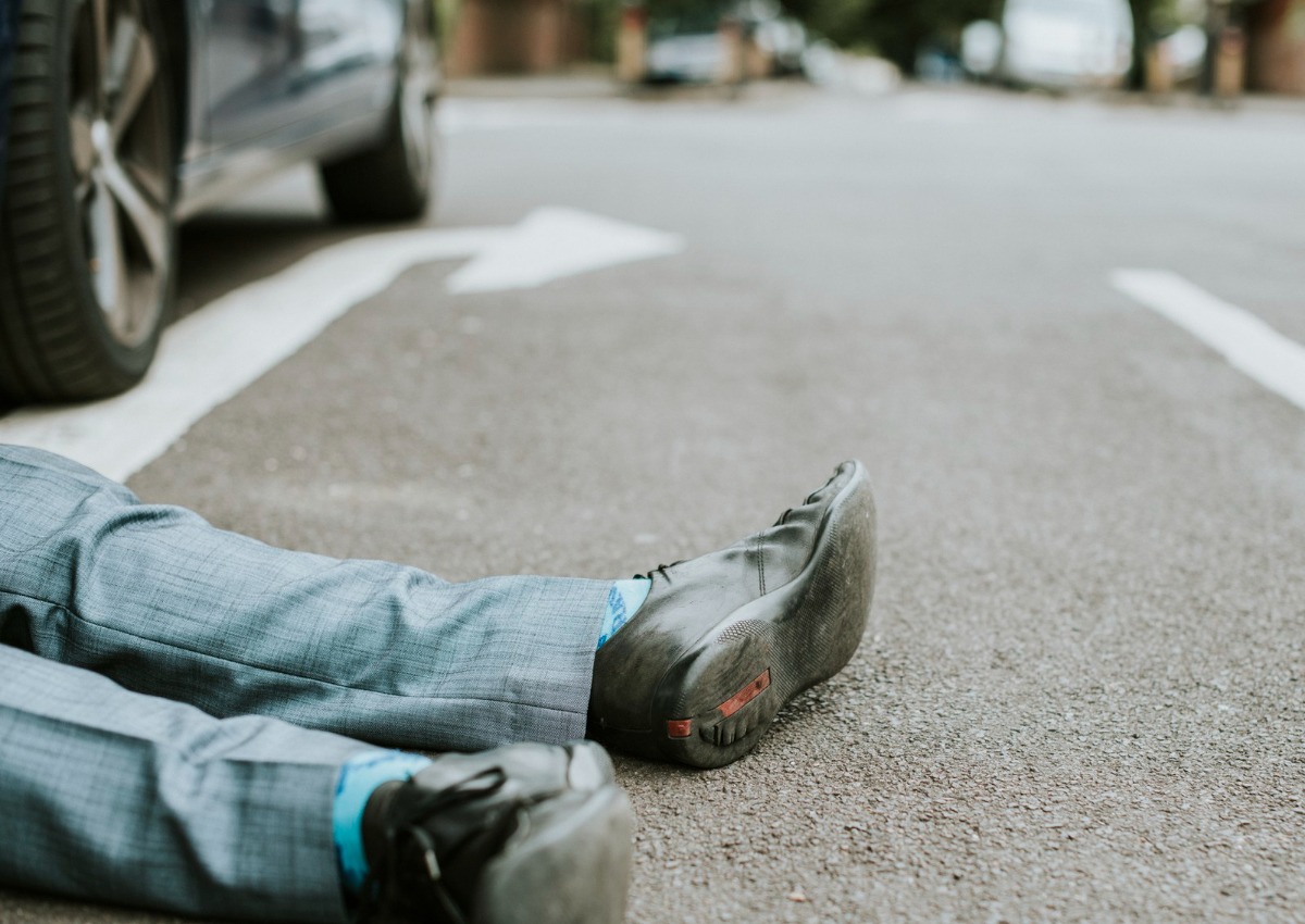 Um homem deitado desmaiado no meio da rua, com carros ao fundo